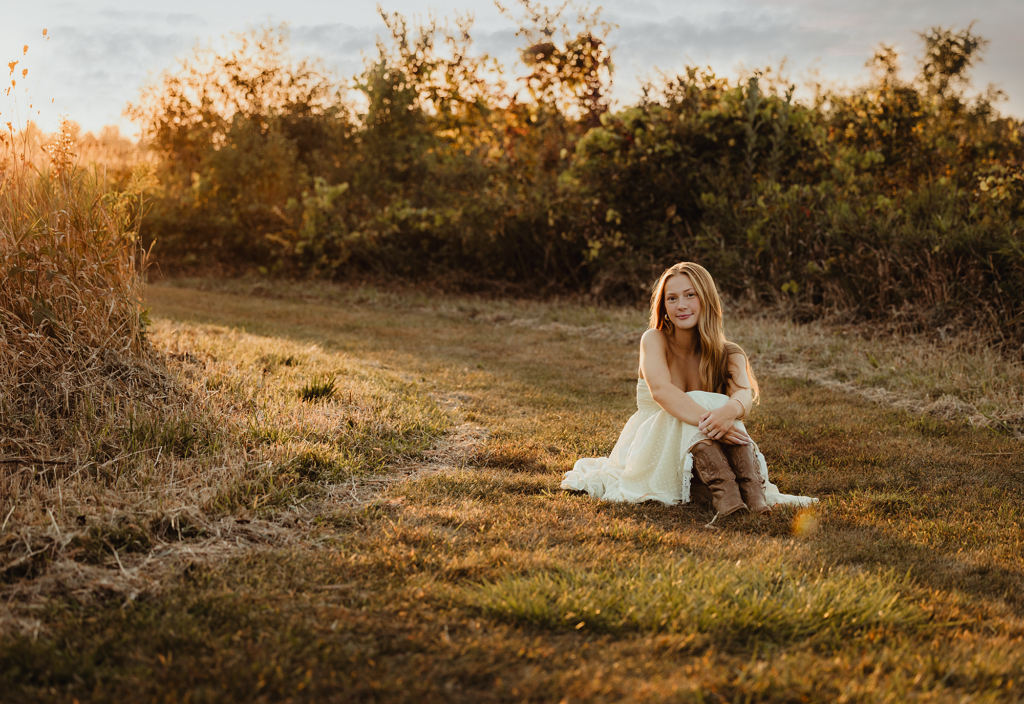 High school senior sitting on a grassy path during a golden hour senior photography session at Burnidge Forest Preserve in Elgin, Illinois.