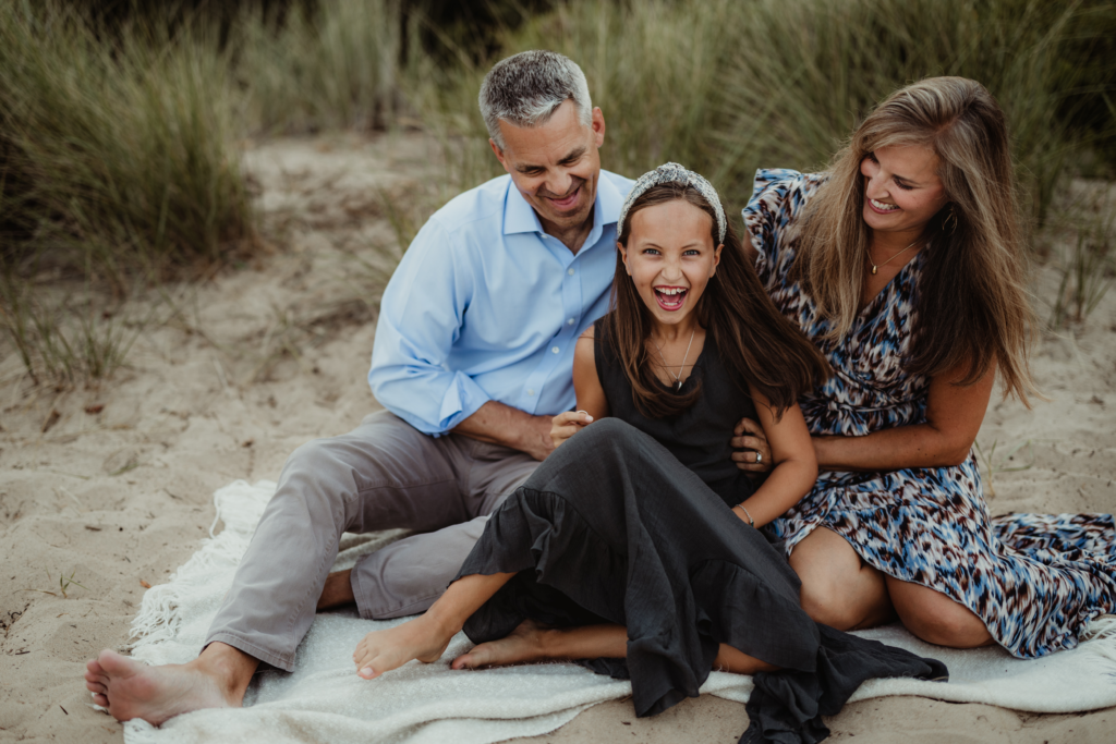 Parents and their daughter laughing together during a candid outdoor family portrait session on a sandy beach in the Chicagoland area, photographed by LibbyLou Images.