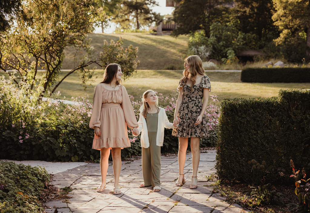Three sisters walking hand in hand through the gardens during a family photography session at Fabyan Forest Preserve in Geneva, Illinois.