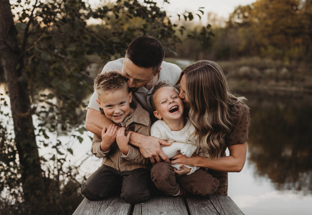 Parents hugging and laughing with their two young sons on a wooden dock at Rolling Knolls Forest Preserve.