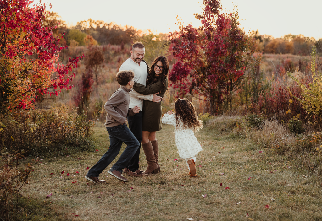 Parents hugging while their children run toward them during a family session at Schweitzer Woods Forest Preserve in Sleepy Hollow, Illinois.