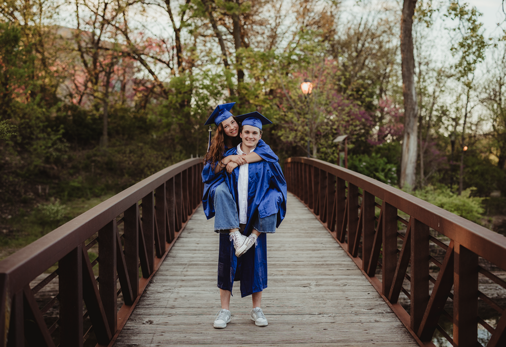 Two Central High School graduates in blue caps and gowns standing on a wooden bridge in Downtown Batavia