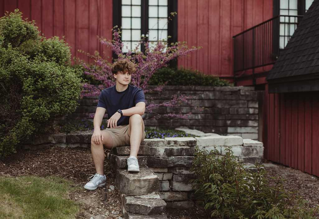 Batavia High School senior sitting on stone landscaping in front of the red Batavia Depot Museum
