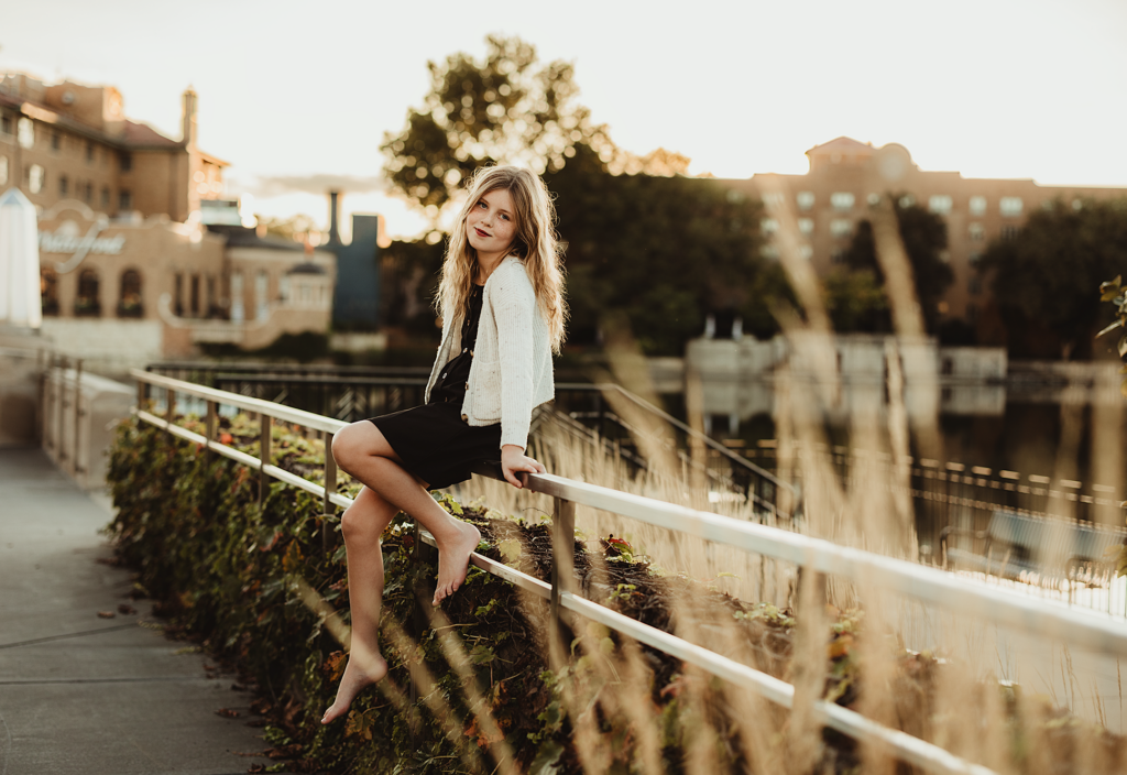Young girl sitting on a railing overlooking the Fox River during a portrait session in downtown St. Charles, Illinois.