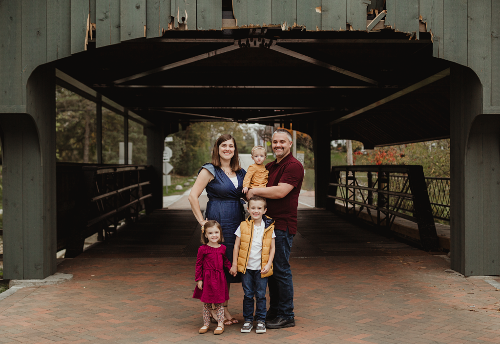 Family of five standing beneath the covered bridge in Historic Long Grove, Illinois.
