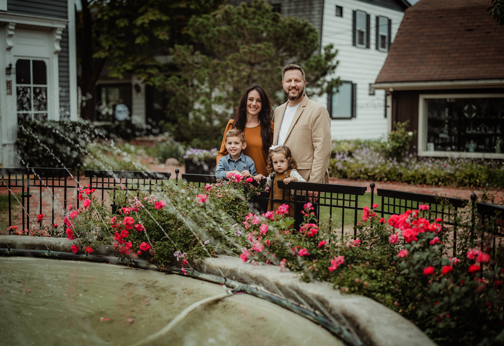 Family of four posing beside the flower-lined fountain in Historic Long Grove, Illinois.