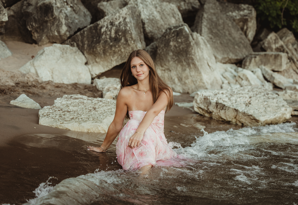 High school senior sitting on shoreline rocks at Lighthouse Beach in Evanston, IL during golden hour.