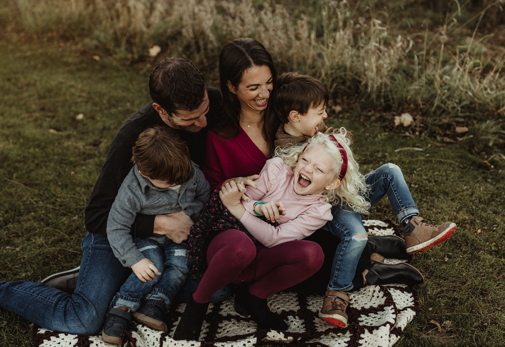 Family laughing together while sitting on a blanket during an outdoor photo session at Vehe Farm Park