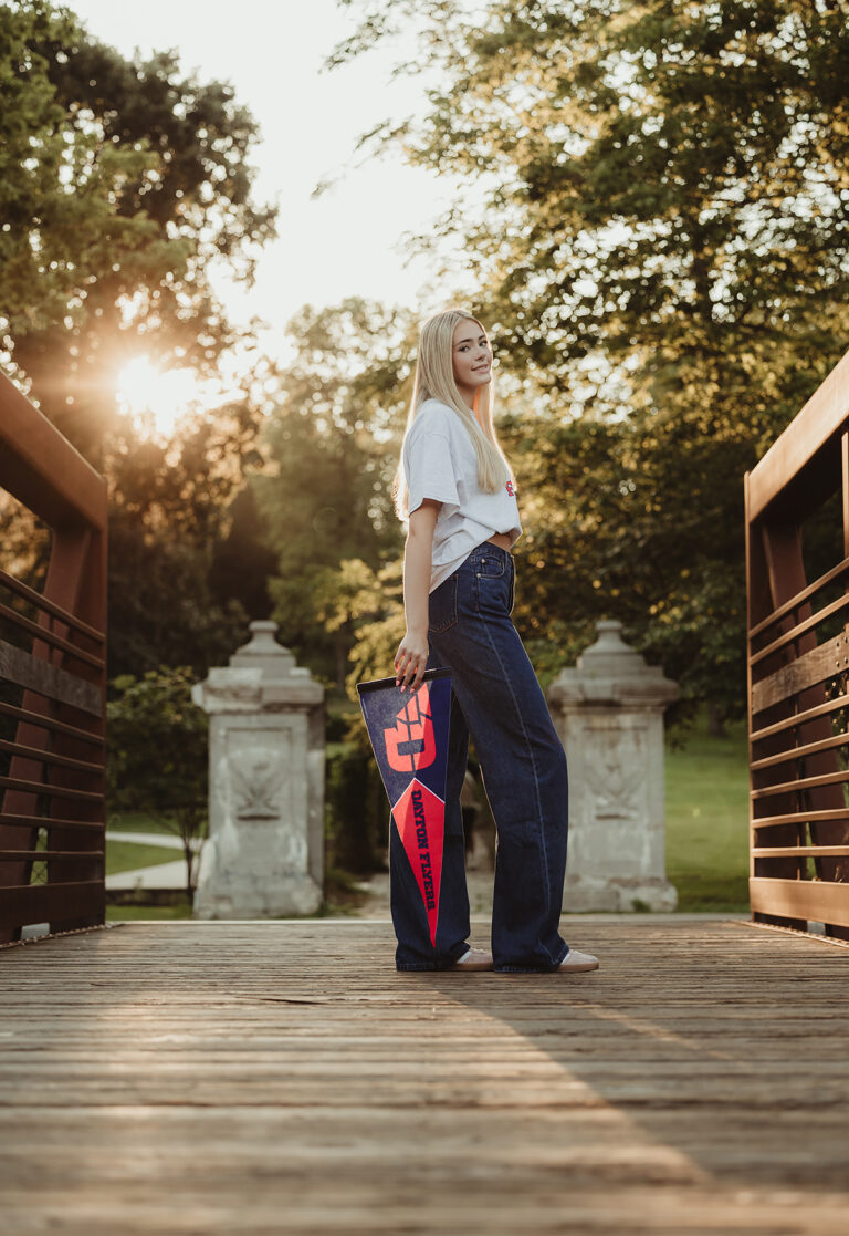 Central High School senior holding a University of Dayton Flyers pennant on the bridge at Fabyan Forest Preserve