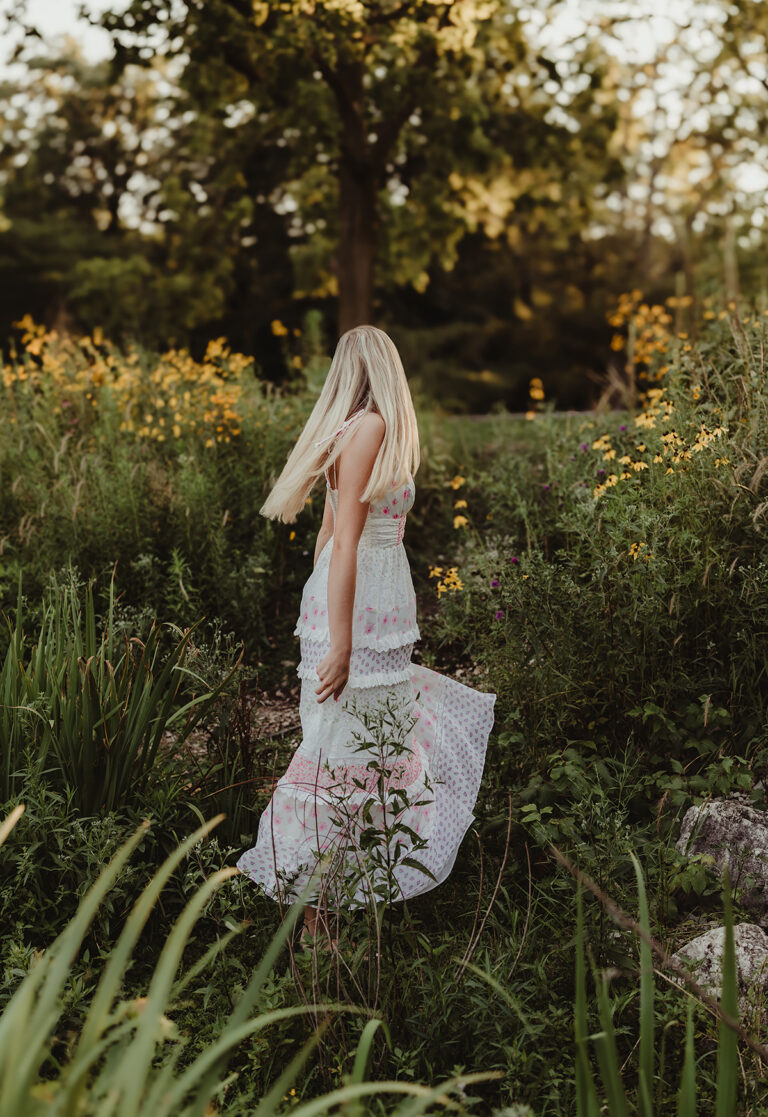 Central High School senior in a floral maxi dress walking through wildflowers at Fabyan Forest Preserve