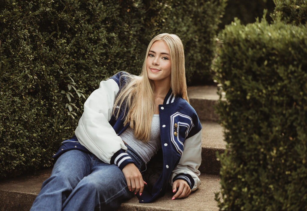 Central High School senior girl posing on garden steps in her navy and white varsity jacket