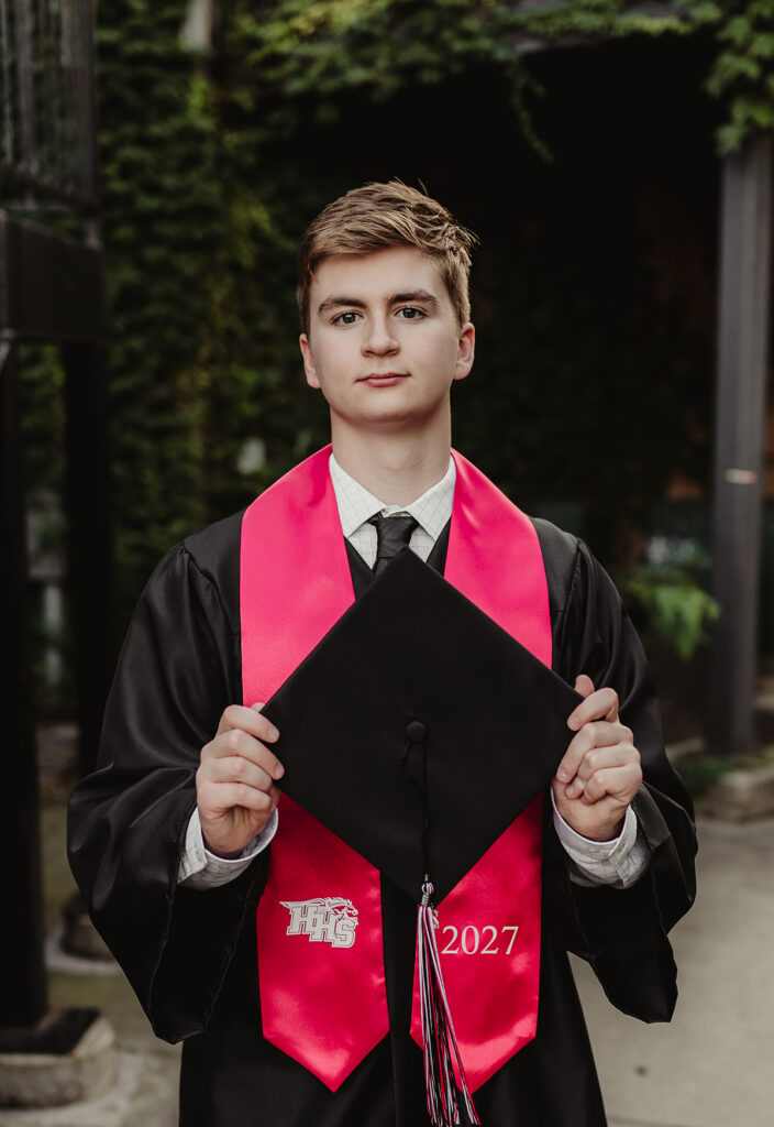 Class of 2027 Huntley High School senior wearing a black graduation gown and red stole while holding his cap