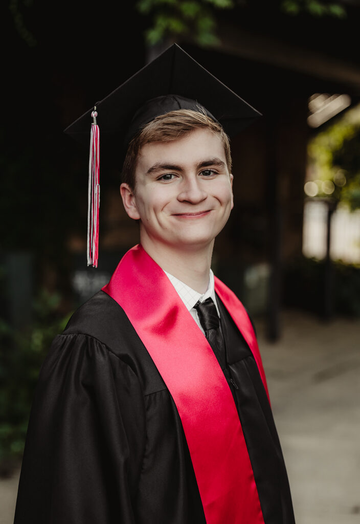 Huntley High School senior Smiling Class of 2027 senior wearing his graduation cap, black gown and red stole