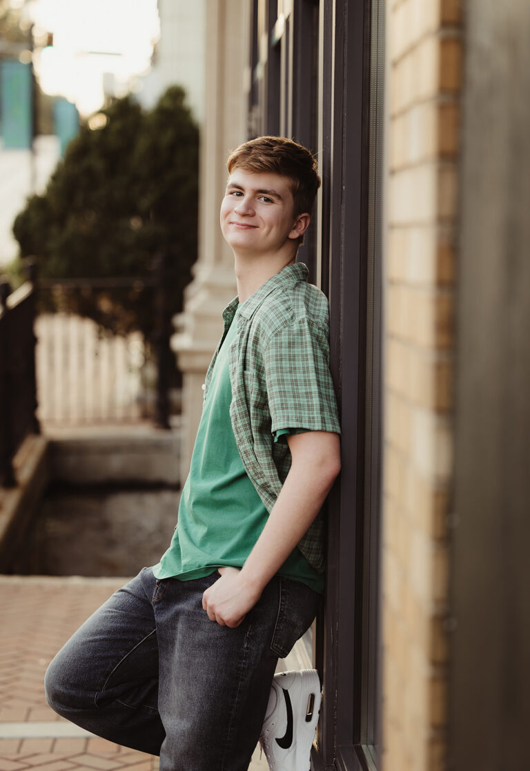 High school senior guy leaning against a downtown storefront during his senior portrait session