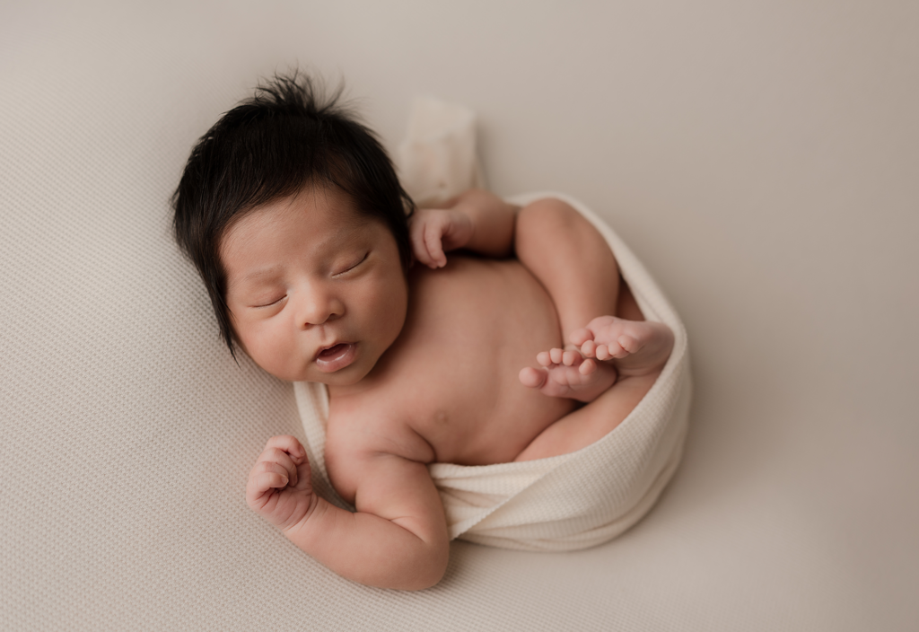 Sleeping newborn baby wrapped in cream during a newborn photography session in Elgin, Illinois