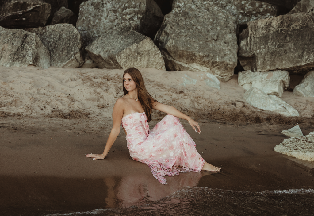 Central High school senior in a pink floral dress sitting along the rocky shoreline at Lighthouse Beach in Evanston, Illinois