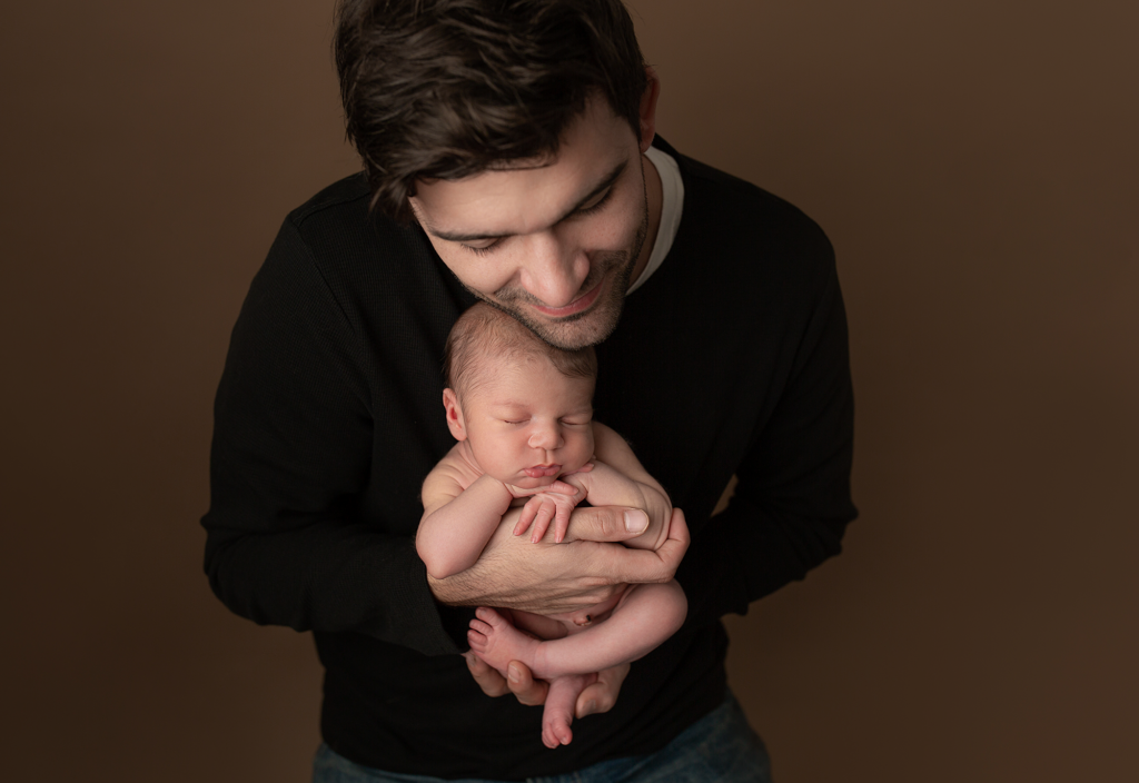 Father holding his sleeping newborn during a warm studio newborn session