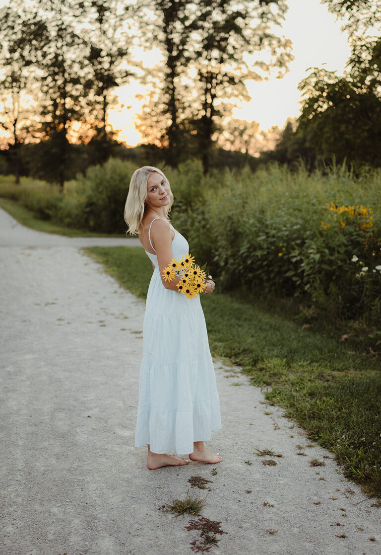 Hampshire High School senior holding yellow wildflowers on a prairie trail at LeRoy Oakes Forest Preserve