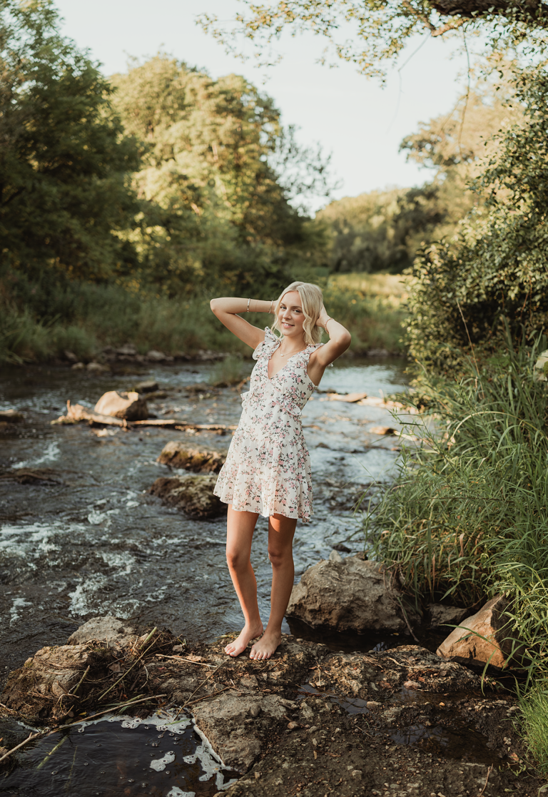 Hampshire High School senior in a floral dress standing barefoot beside the creek at LeRoy Oakes Forest Preserve