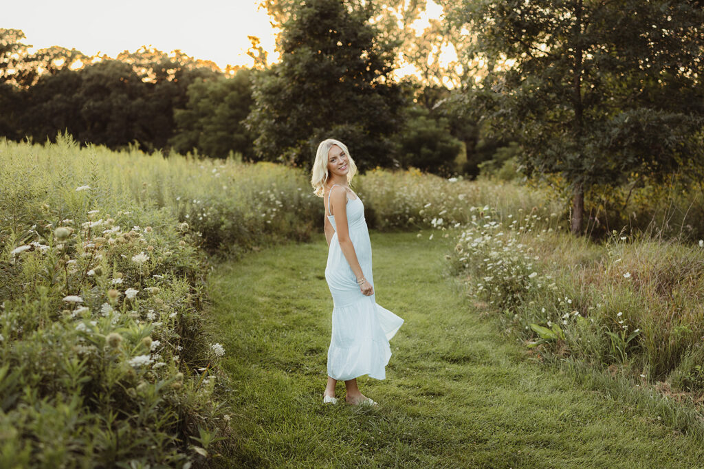 Hampshire High School senior standing on a grassy prairie path in a light blue dress at sunset