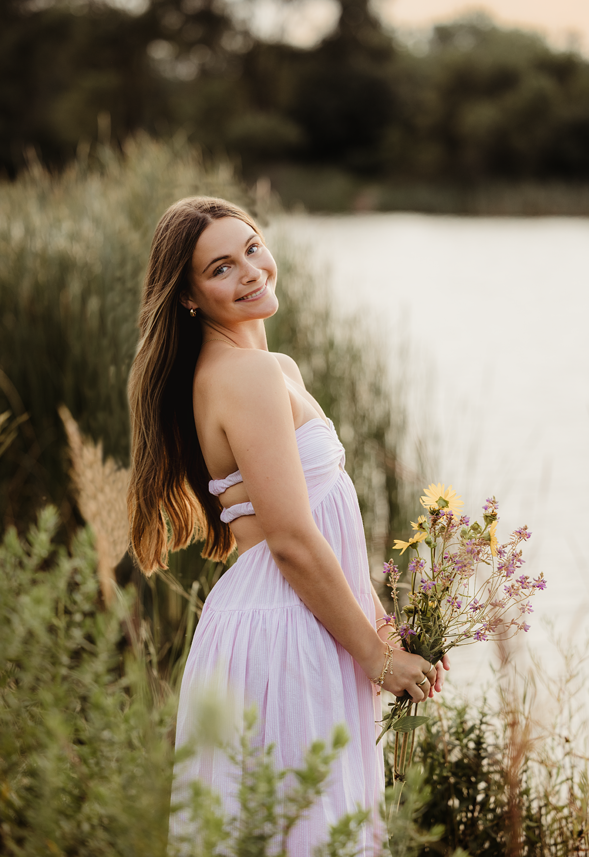 Central High School senior holding wildflowers beside the water at Mallard Lake in Hanover Park during her senior portrait session
