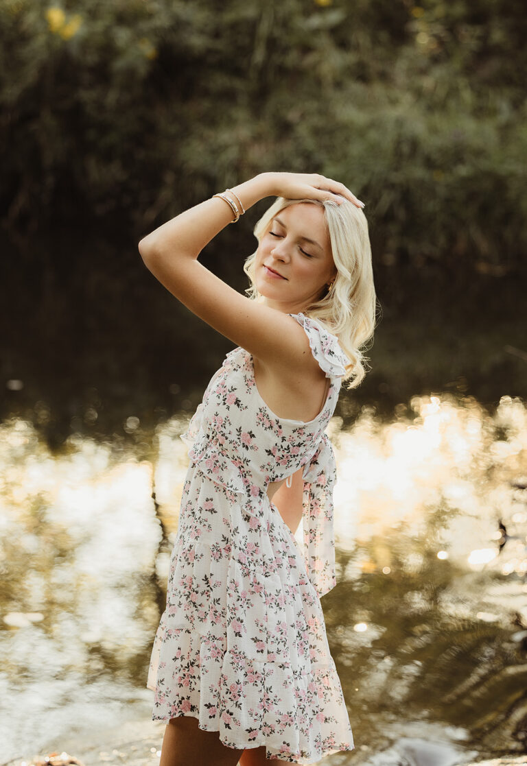 High School senior wearing a floral dress and sitting beside the creek at LeRoy Oakes Forest Preserve