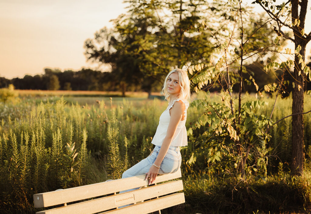 Hampshire High School senior sitting on a bench surrounded by prairie grasses in golden evening light