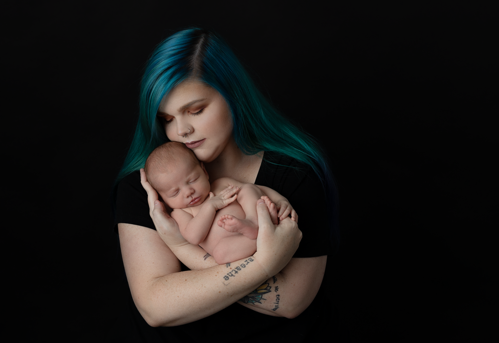 Mother kissing her sleeping newborn during a black background