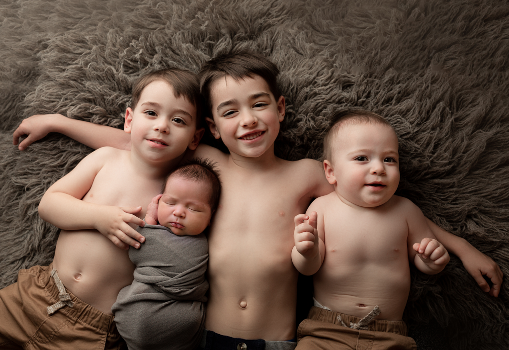 Four brothers lying together with their swaddled newborn sibling during an Elgin newborn photography session