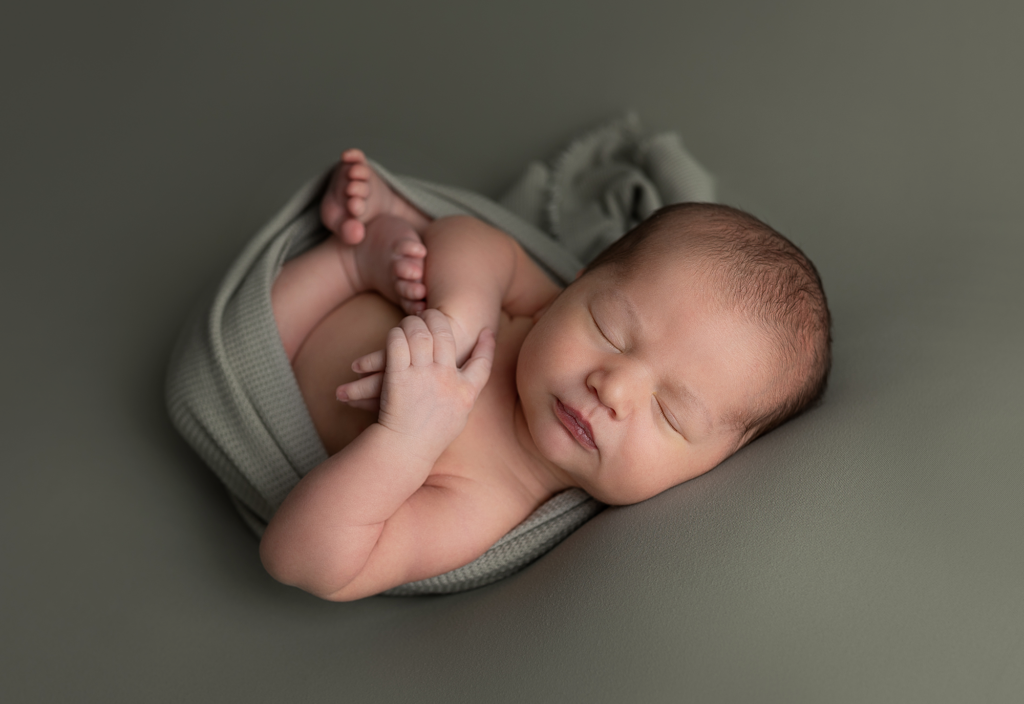 Sleeping newborn baby boy posed in sage green on a coordinating studio backdrop