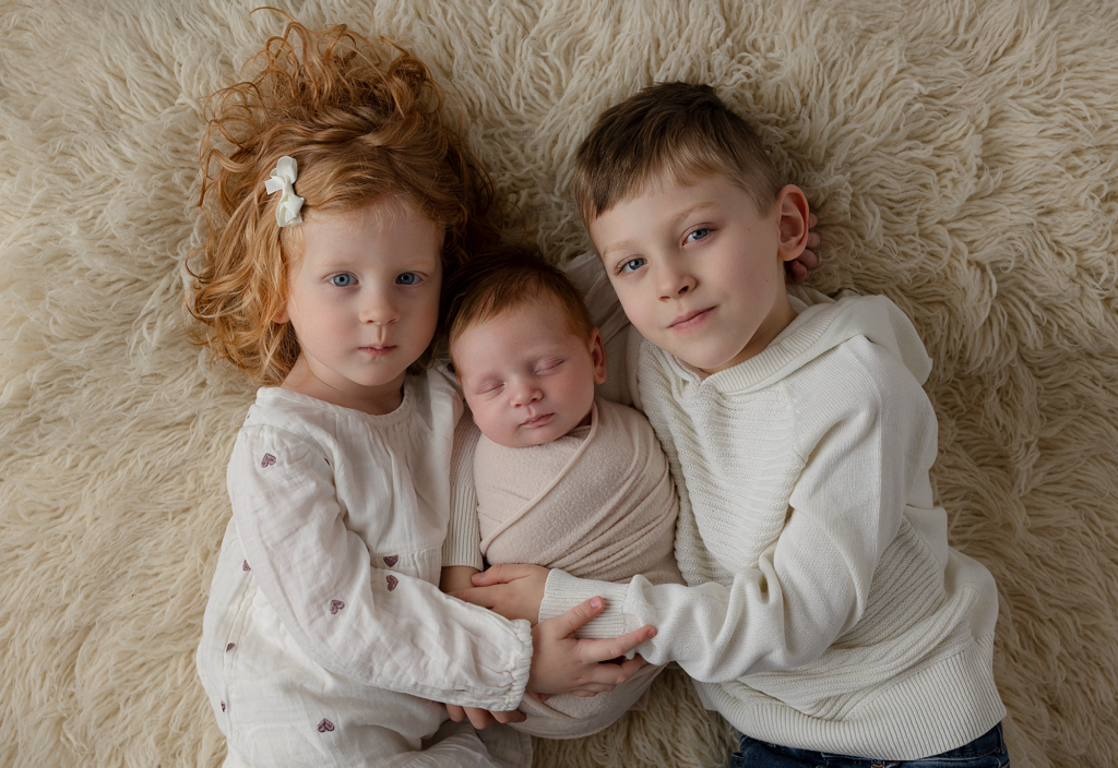 Three siblings cuddling their newborn baby during a studio newborn photography session in Elgin, Illinois
