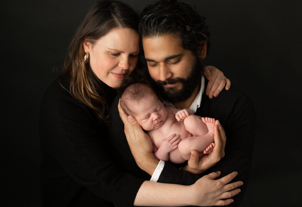 Parents embracing their sleeping newborn during a black background studio portrait