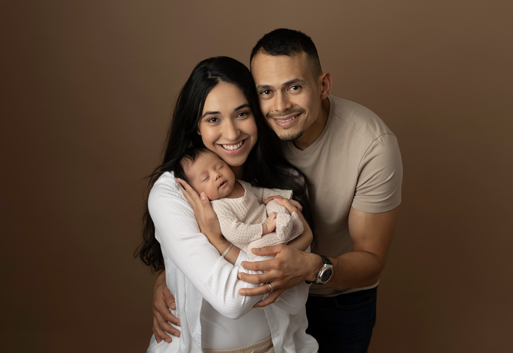Smiling parents holding their sleeping newborn during a studio newborn session