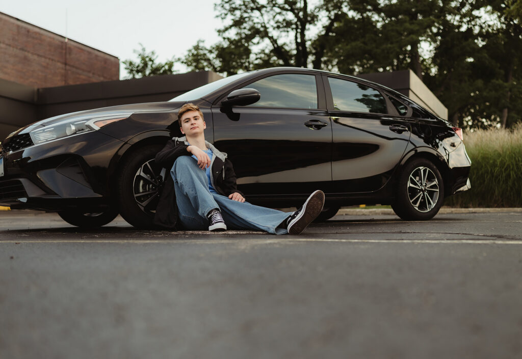 Huntley High school senior sitting beside his black car during an urban senior photography session