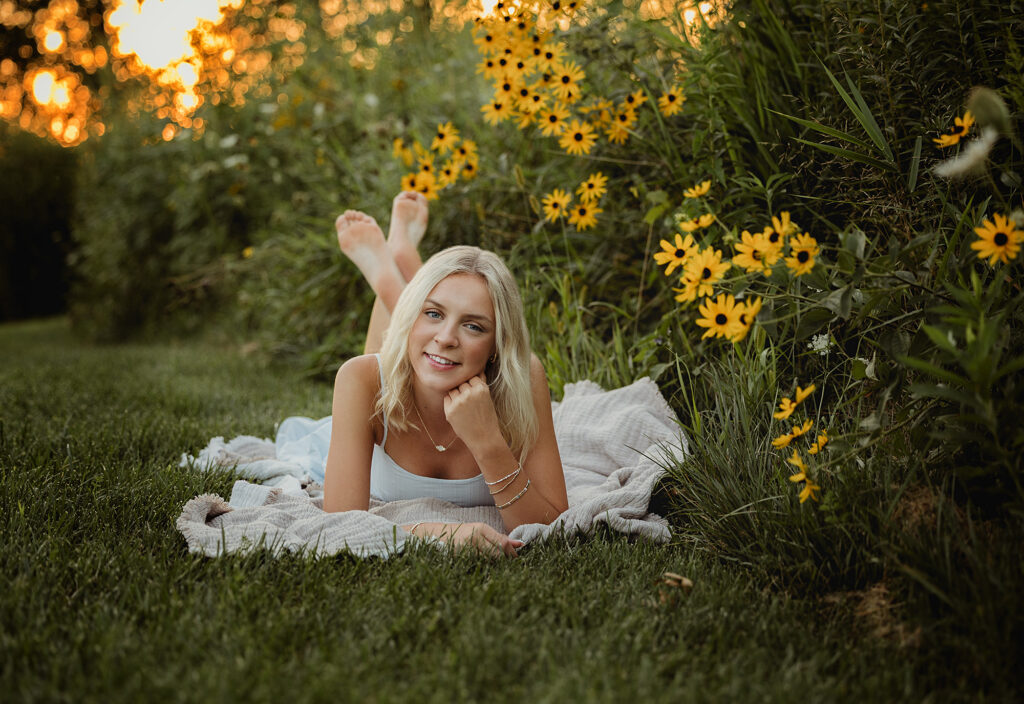 Hampshire High School senior lying on a blanket beside yellow wildflowers during her summer senior session