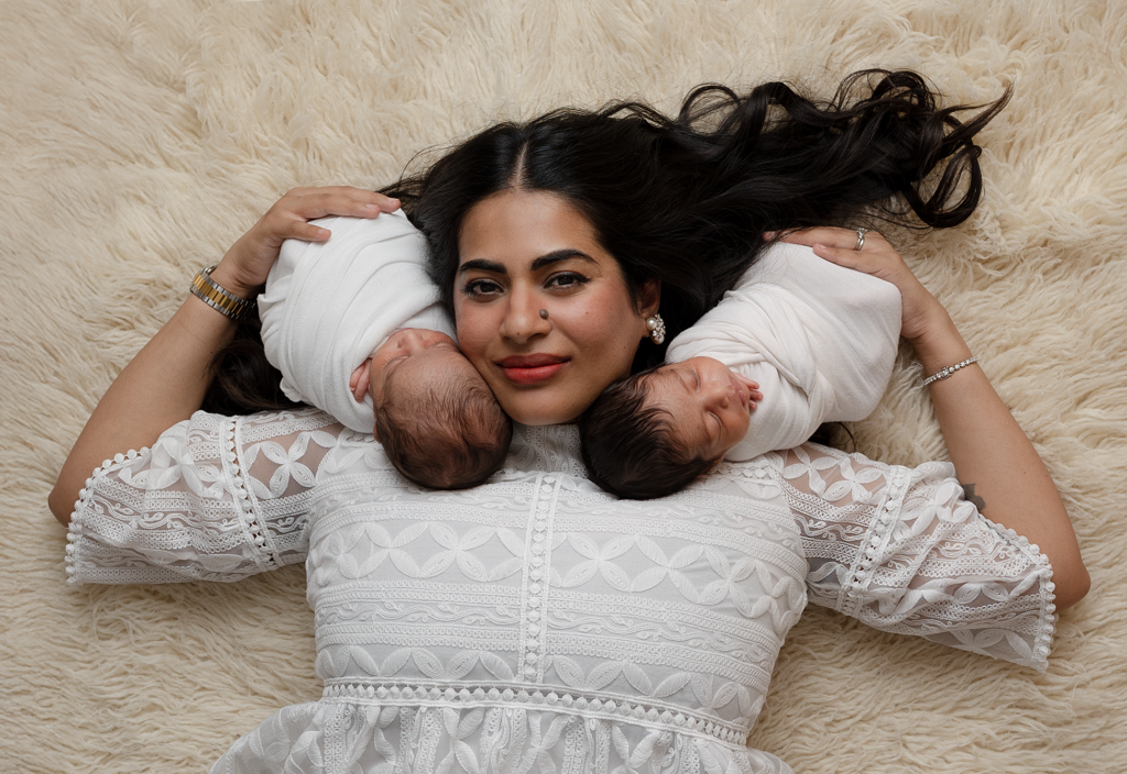Mother lying between her newborn twins during a studio twin newborn session