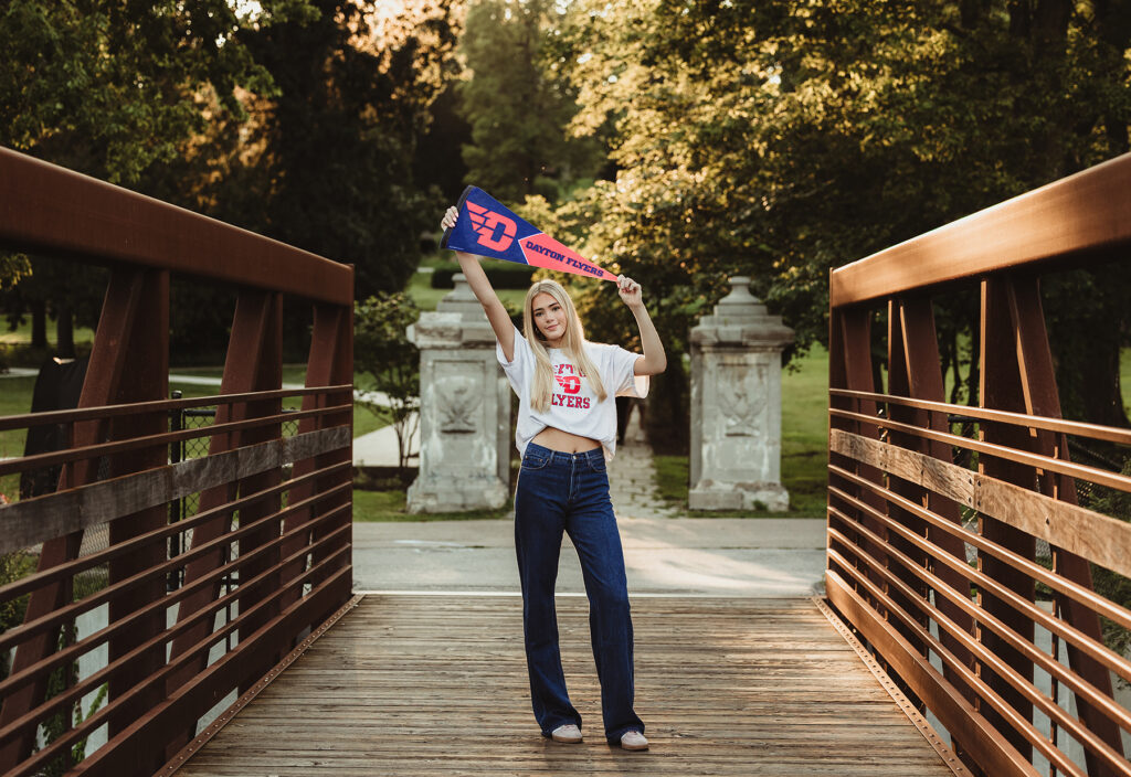 Central High School senior holding a University of Dayton Flyers pennant on the Fabyan Forest Preserve bridge