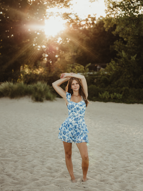 High school senior in blue dress standing on sand at Lighthouse Beach in Evanston, Illinois during sunset photo session