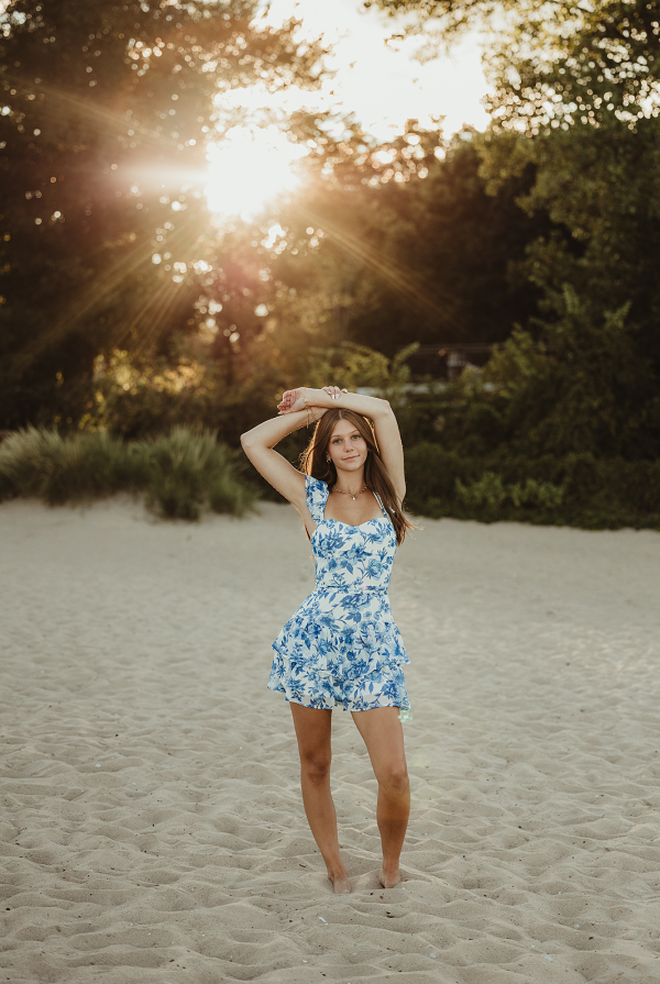 High school senior in blue dress standing on sand at Lighthouse Beach in Evanston, Illinois during sunset photo session