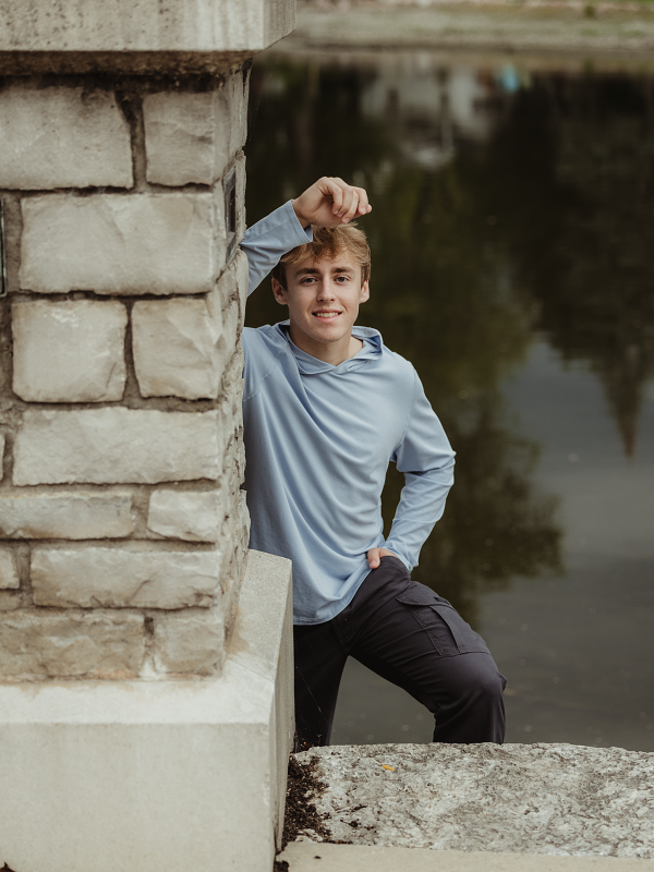 Central High School senior leaning against a stone wall beside the Fox River in Downtown West Dundee.