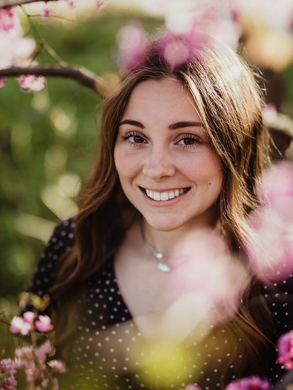 Central High School senior smiling among blooming pink redbud trees at Leroy Oakes Forest Preserve in St. Charles, Illinois.